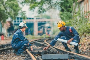 Engineer in safety gear inspects railway track for wear and alignment, ensuring safety standards.
